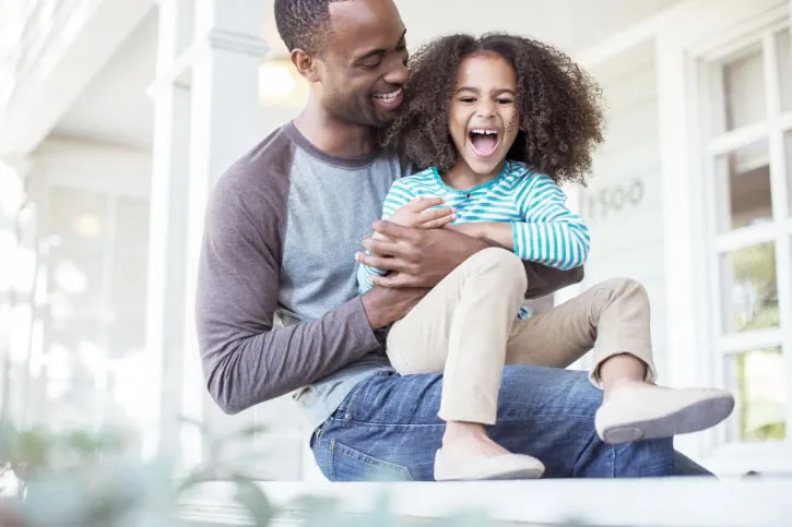 Father tickling daughter on porch.