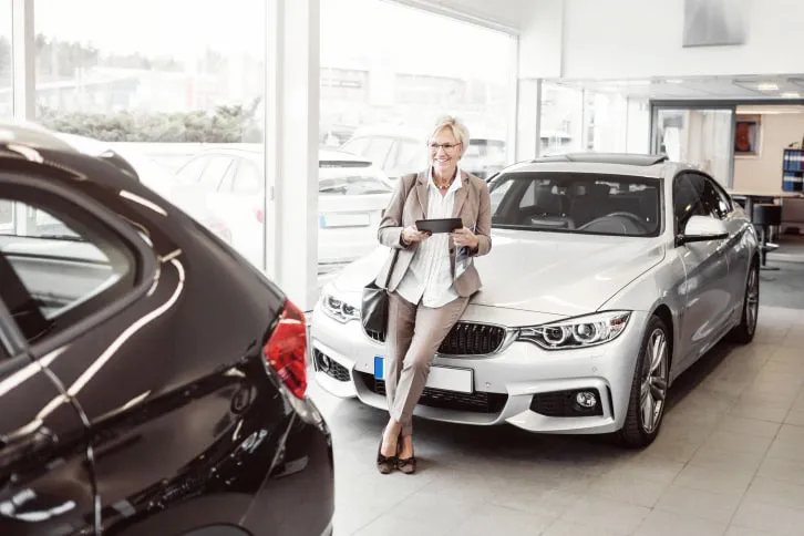 Happy businesswoman with digital tablet looking at car in store