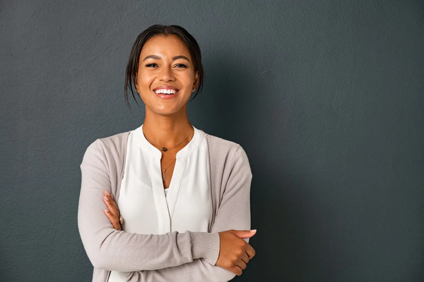 woman with crossed arms and white shirt smiling against dark grey background