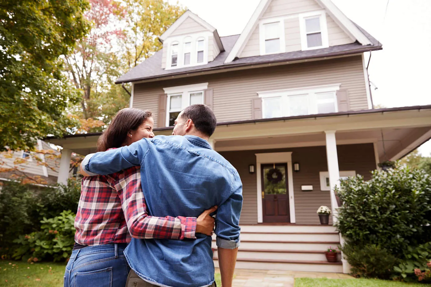 A couple smiles and embraces each other on the front lawn of their new home.