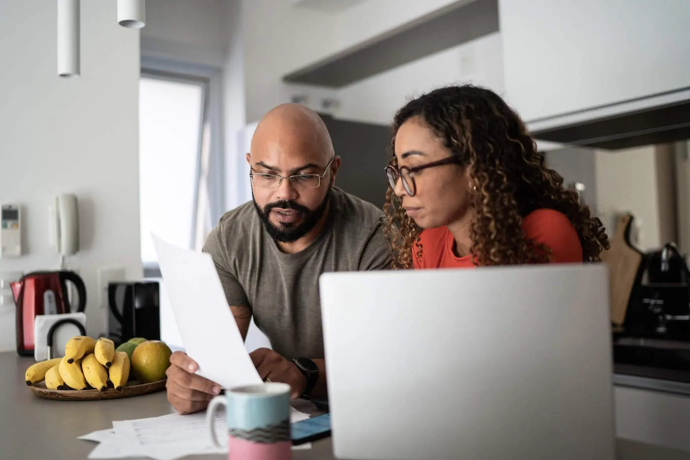 A couple looks at a document together with their laptop next to them at the kitchen counter.