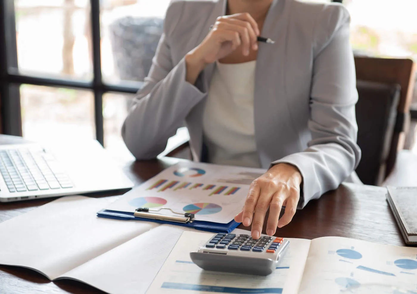 A woman uses a calculator while looking at data chart documents on her desk.