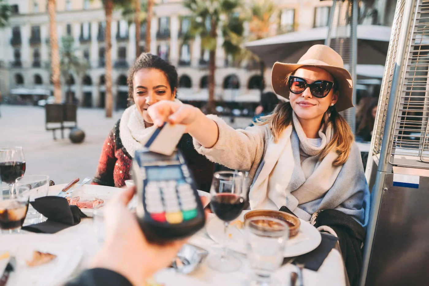 A woman that's wearing a hat and shades taps her credit card to pay for her food at the restaurant.