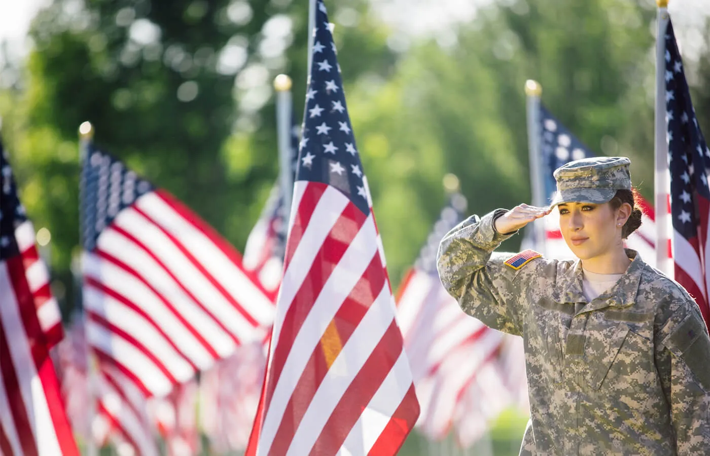 Woman in military uniform salutes next to the US flags