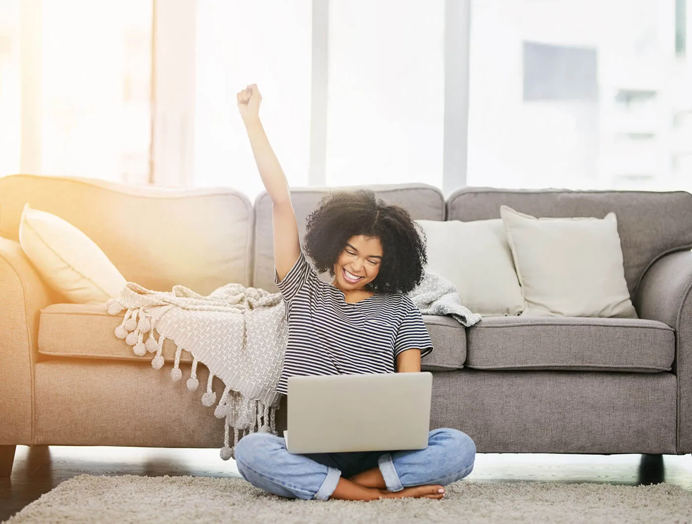 A woman wearing a striped shirt is smiling at her laptop while raising a hand to celebrate.