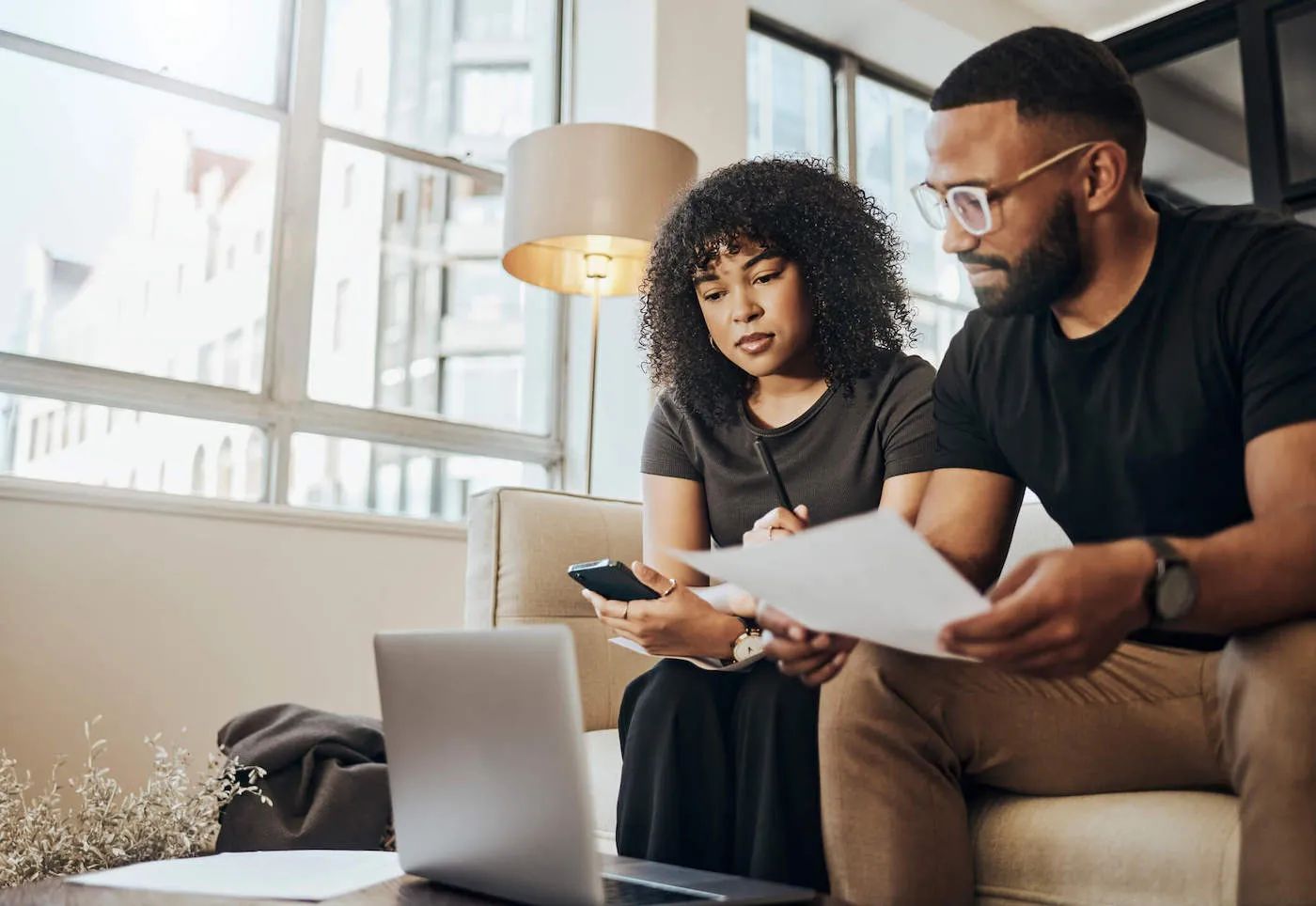 Black couple on sofa at home reviewing savings.