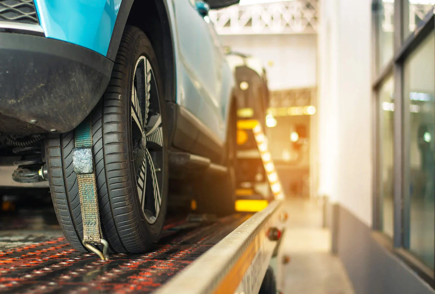 A blue car is strapped in on top of a tow truck.