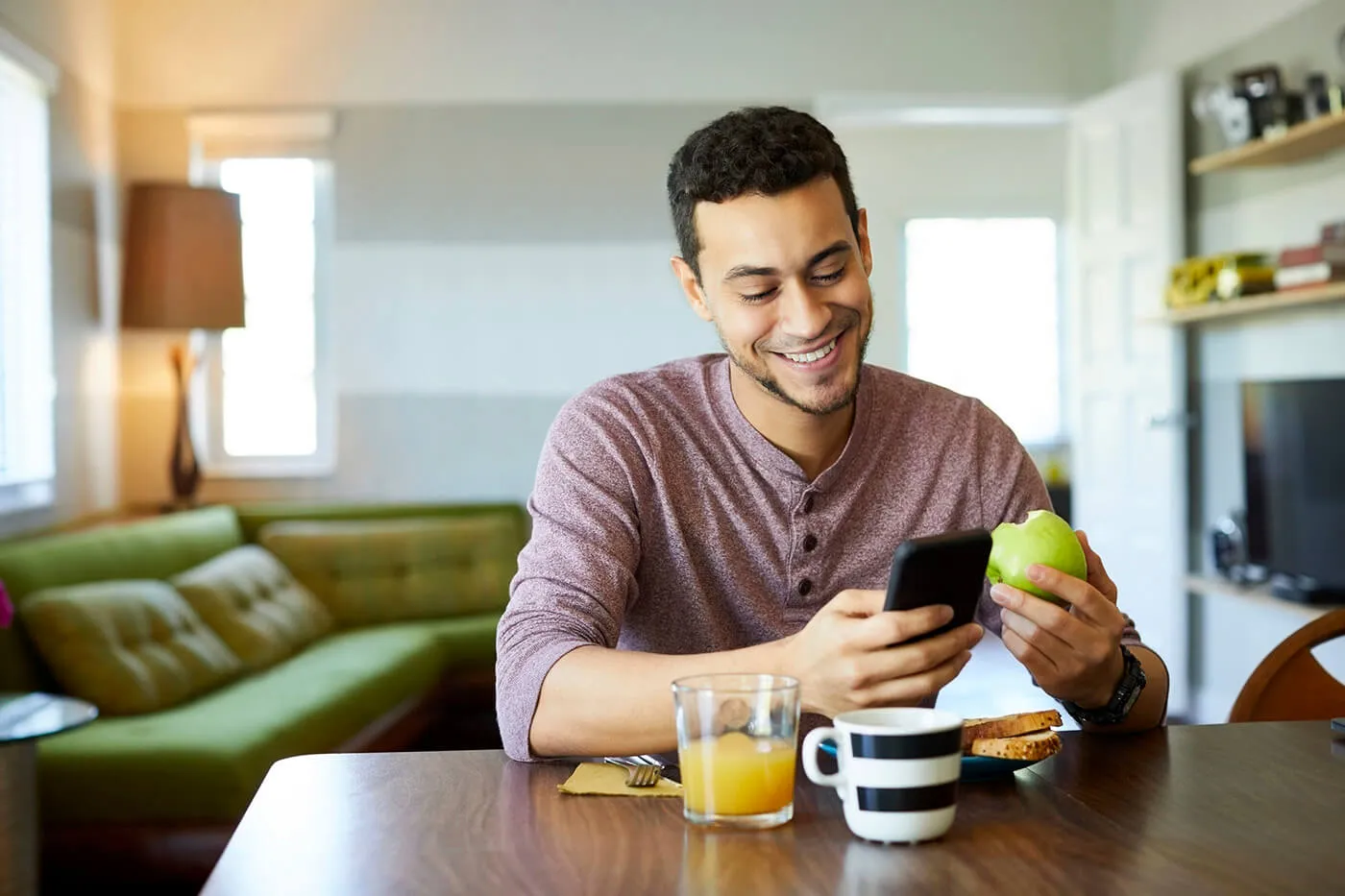 A man looks at his phone while holding an apple in his other hand.