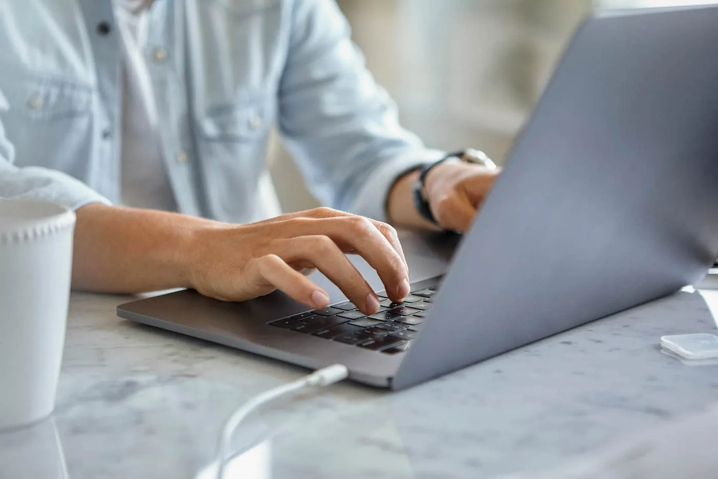 Close up of young man´s hands typing on laptop during daytime.