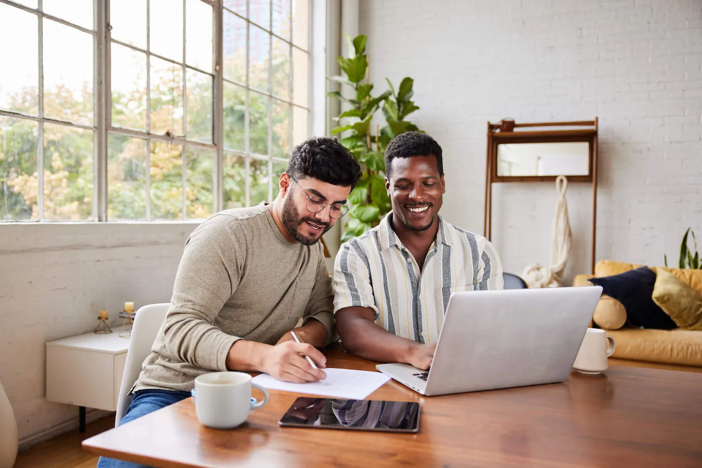 A couple look at a computer together while one of them writes on a document.