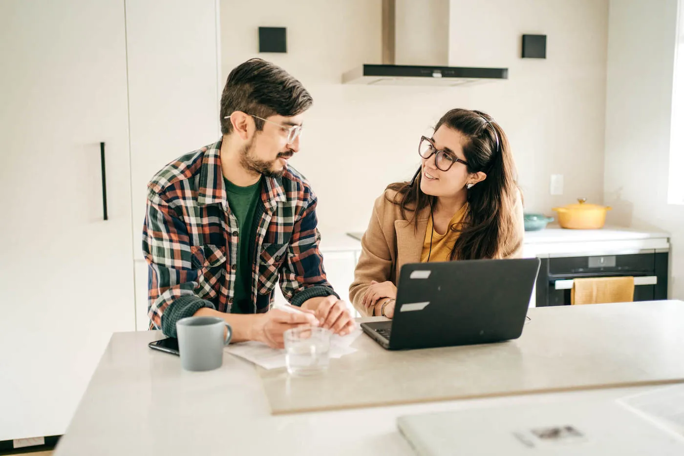 A couple look at each other while their computer sits on the kitchen table.