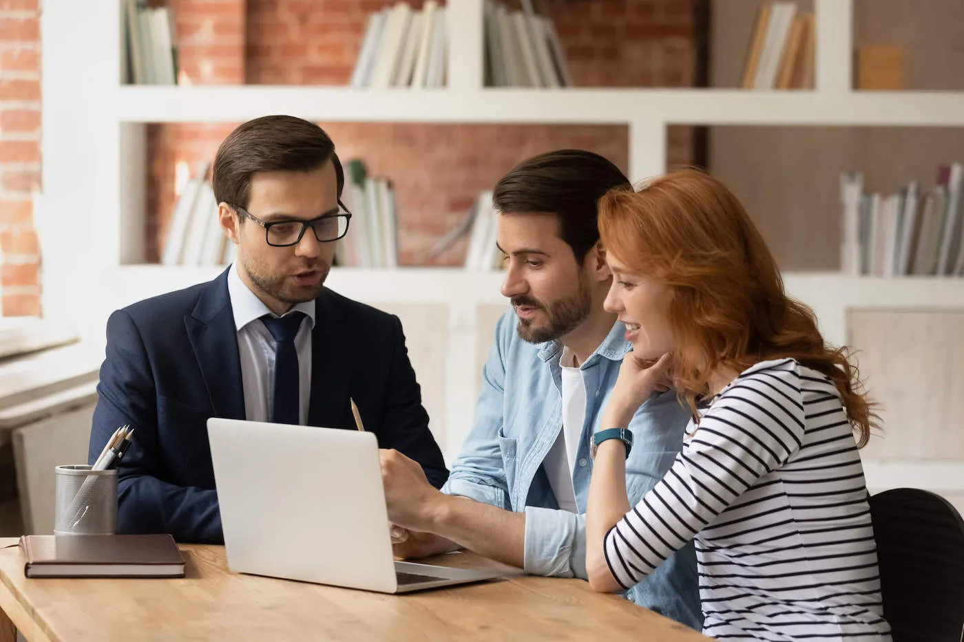 A couple look at a laptop screen while a man in a suit talks to them.