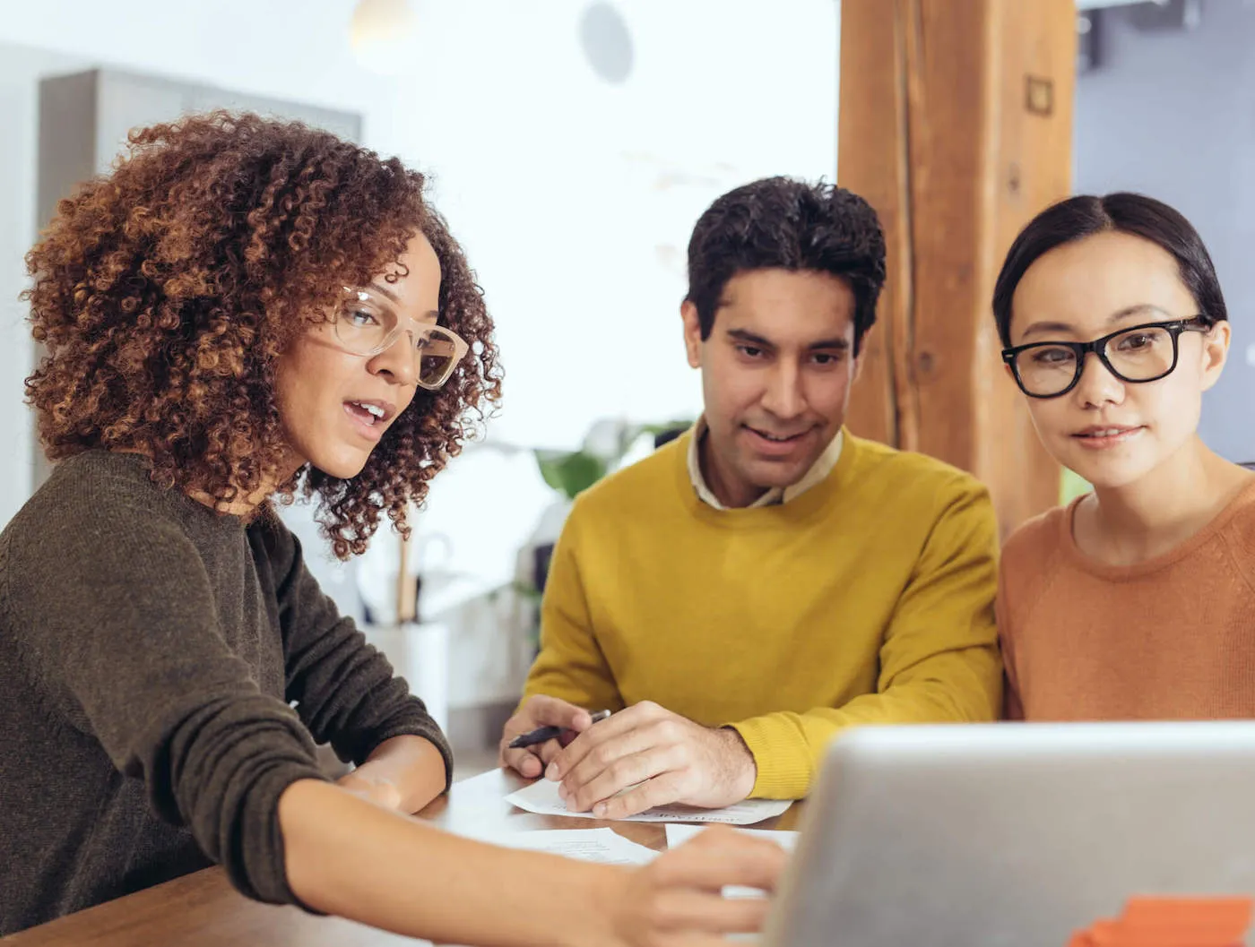 A couple are meeting with an agent with glasses and curly hair who is pointing at a laptop screen.