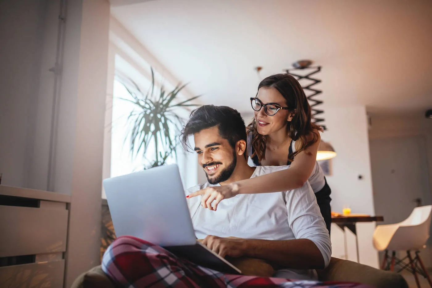 A couple smile and look at a laptop screen together at home.