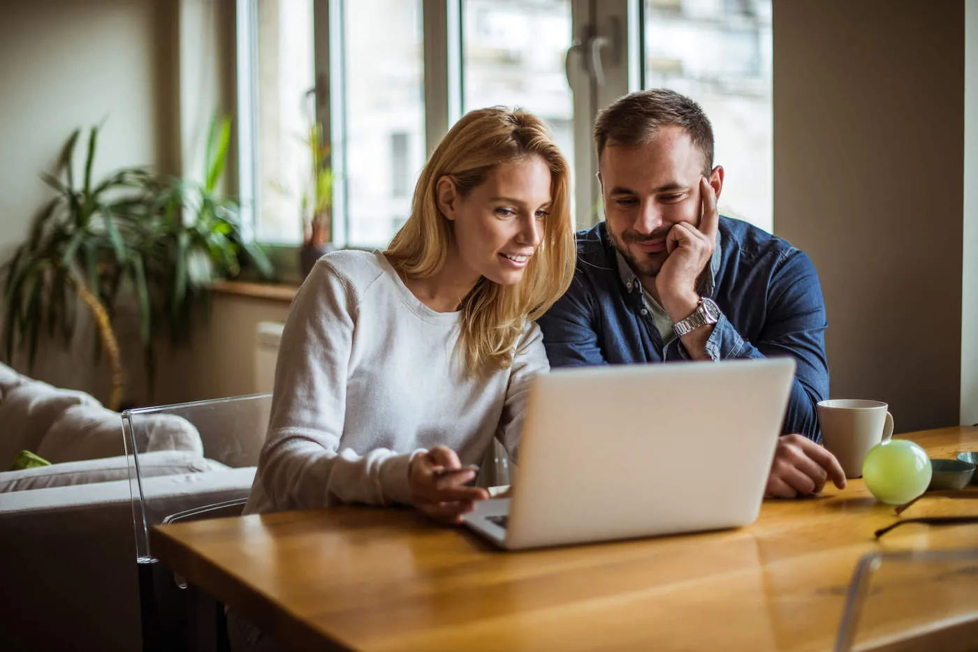 A couple smile at a laptop together while at home.