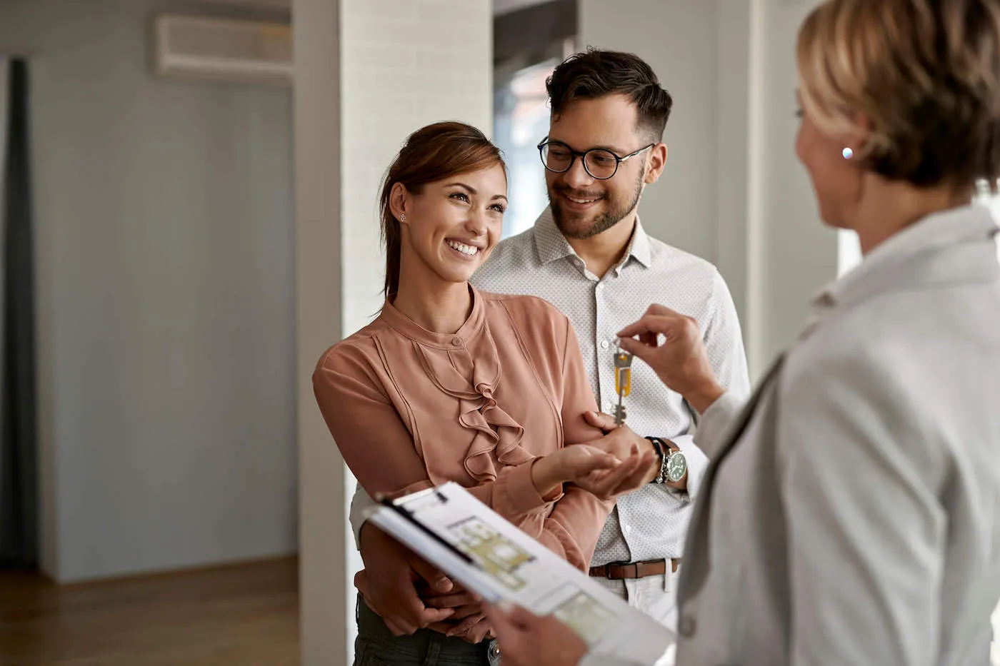 A couple smile together as the realtor gives them the keys to their new apartment.