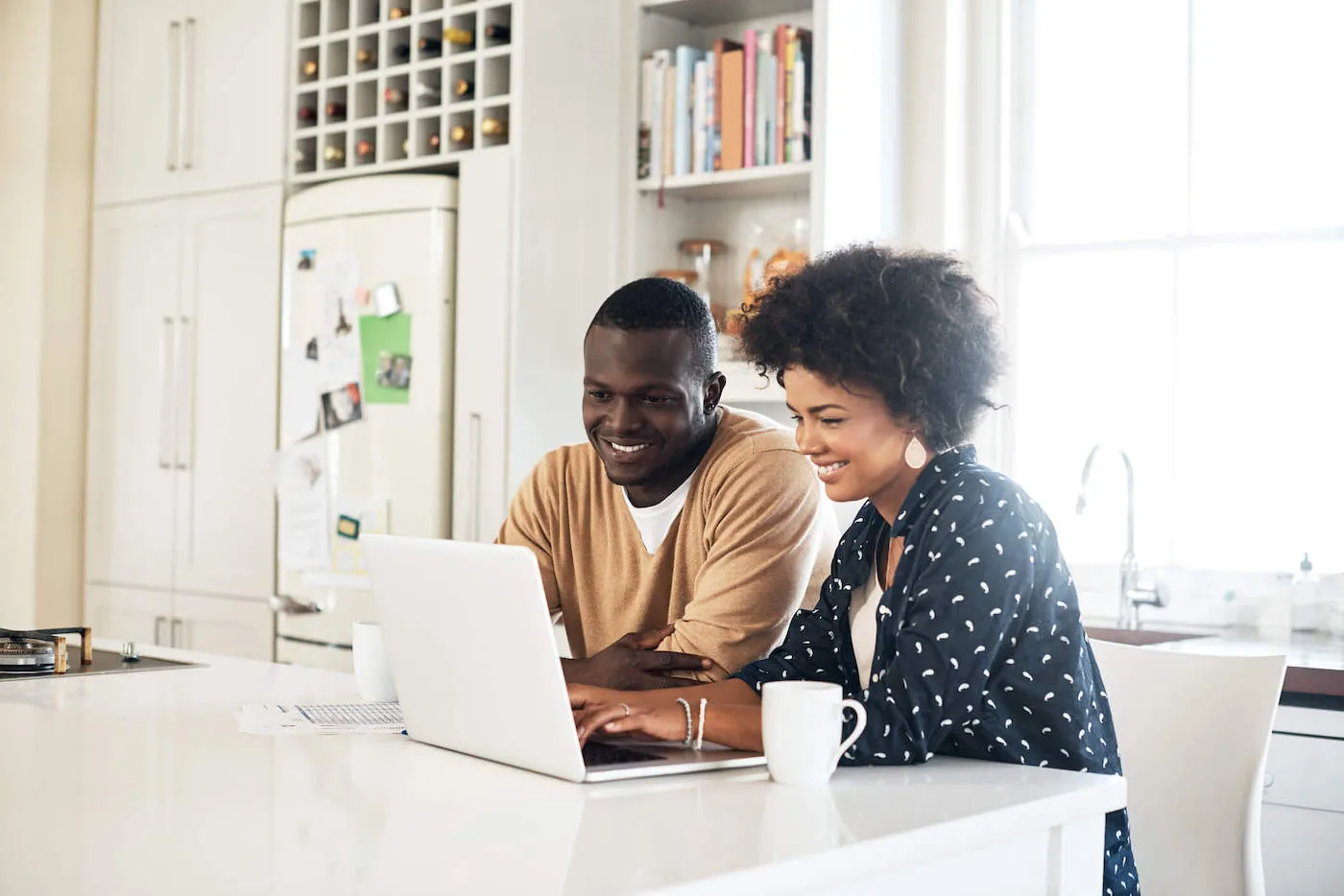 Couple smiles while looking at their laptop computer at the kitchen counter.