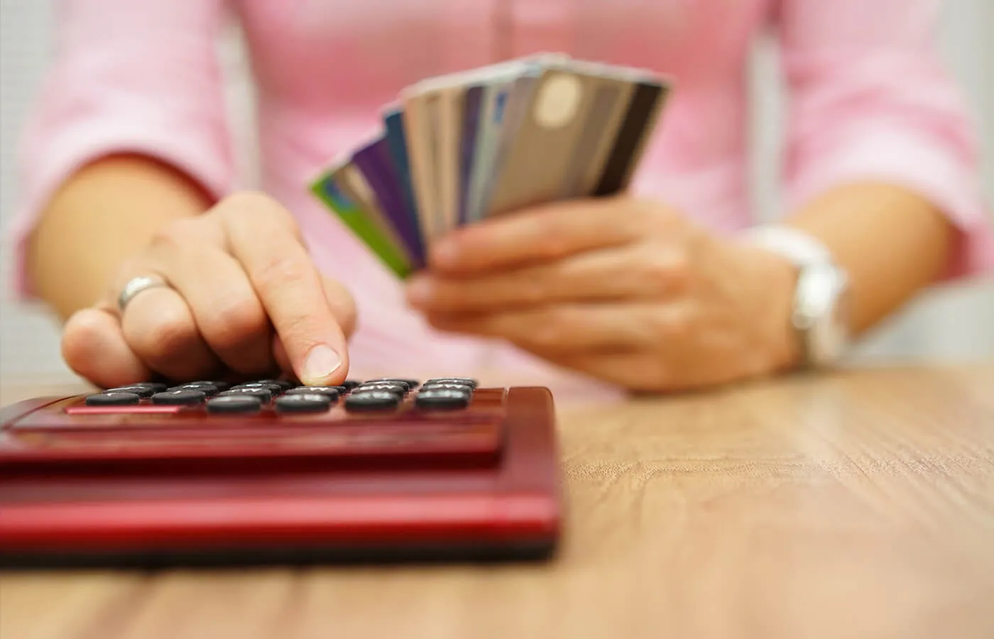 person in pink shirt holding multiple cards and pressing with a finger on a calculator