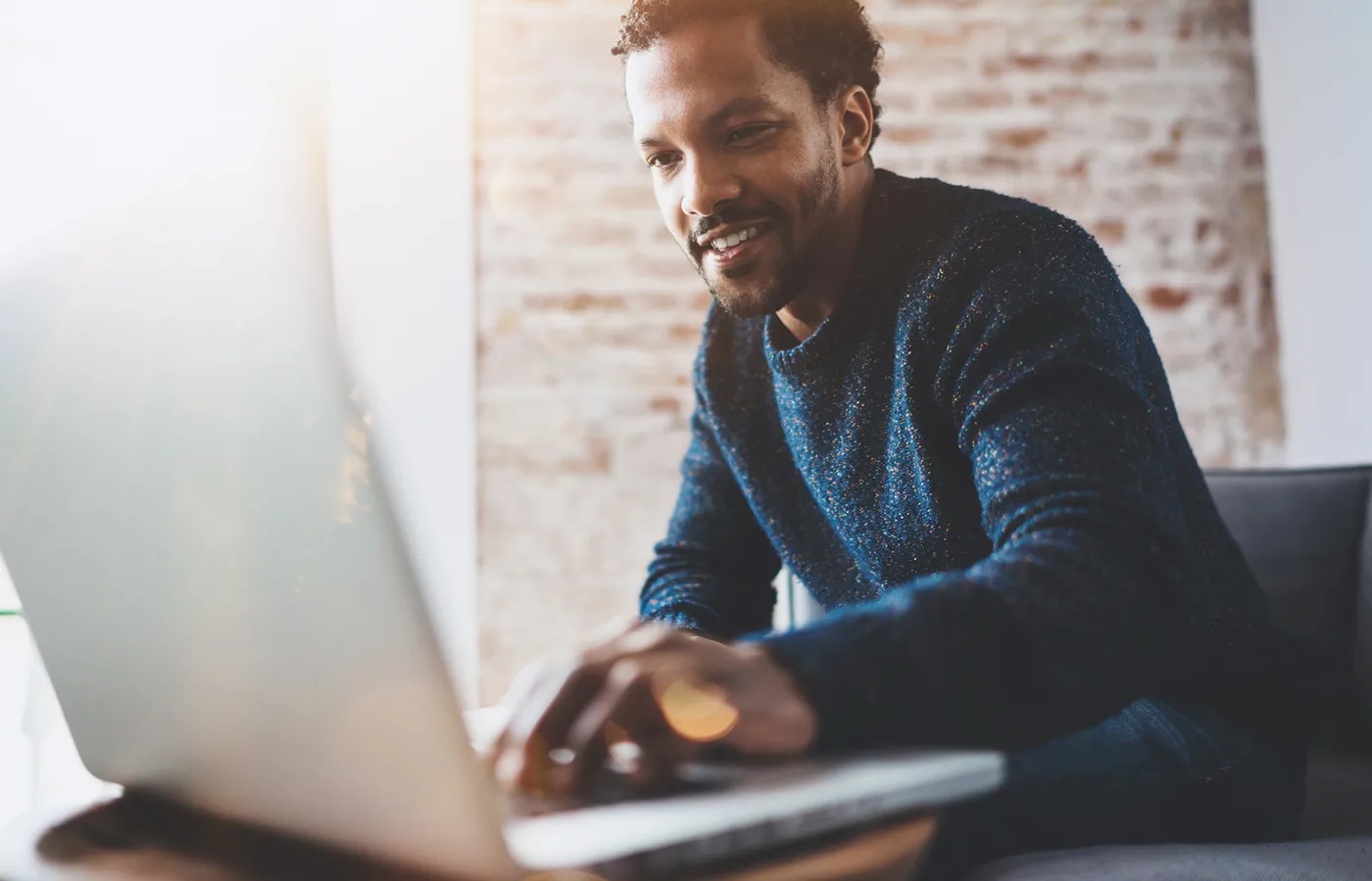 man in dark blue long-sleeve typing on laptop smiling