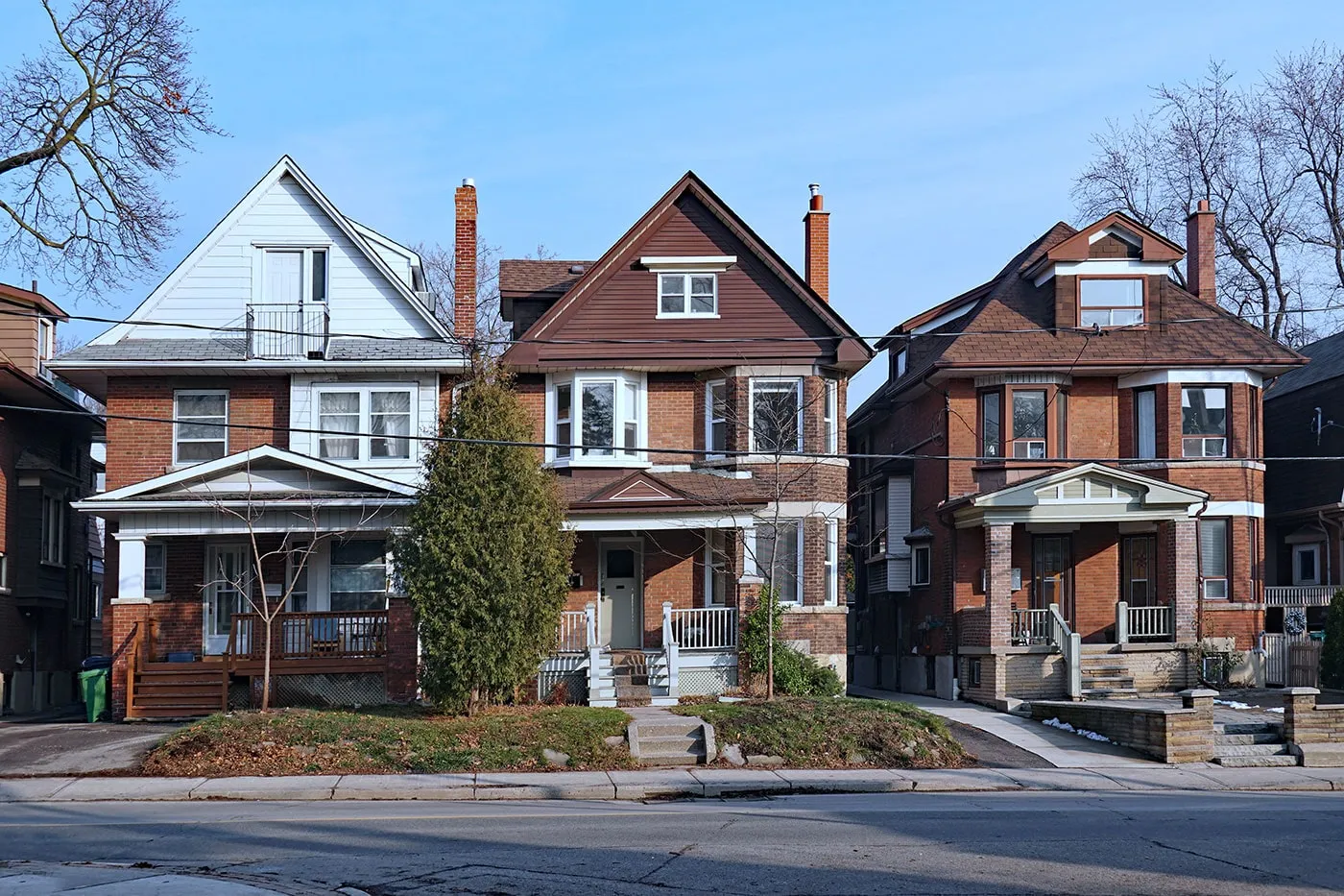 A set of three houses made of brick next to a street.