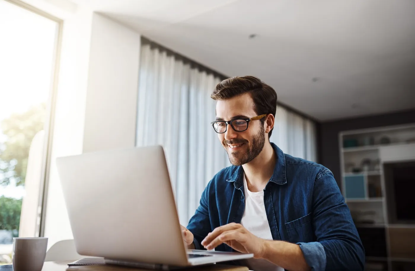 Shot of a smiling man sitting down and using his laptop to research ETFs and mutual funds.