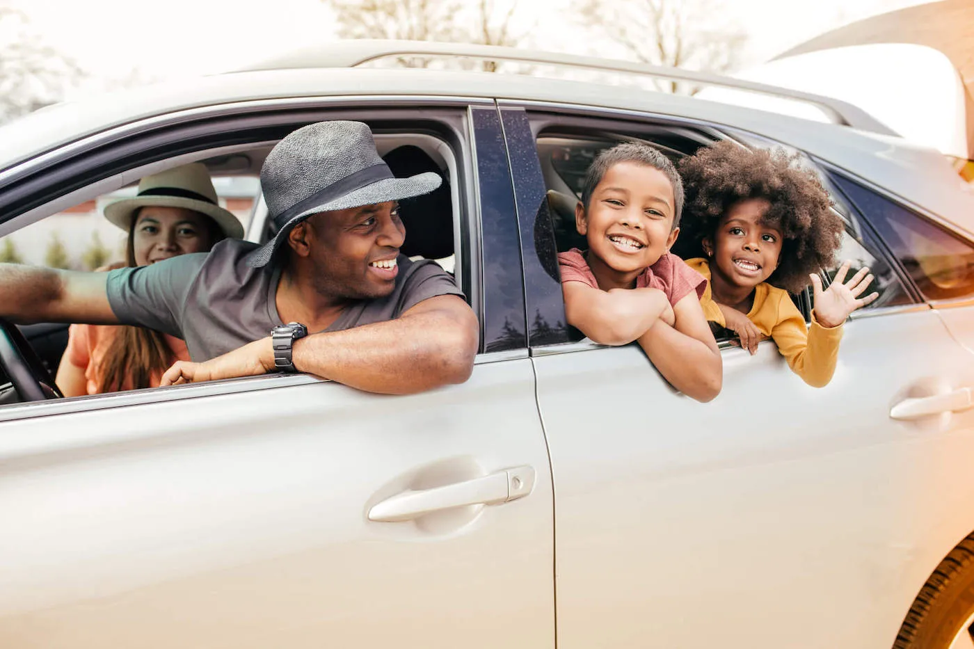 A family of four is looking out their window with the dad and mom in the front seat while their two sons smile and wave hello to the camera.