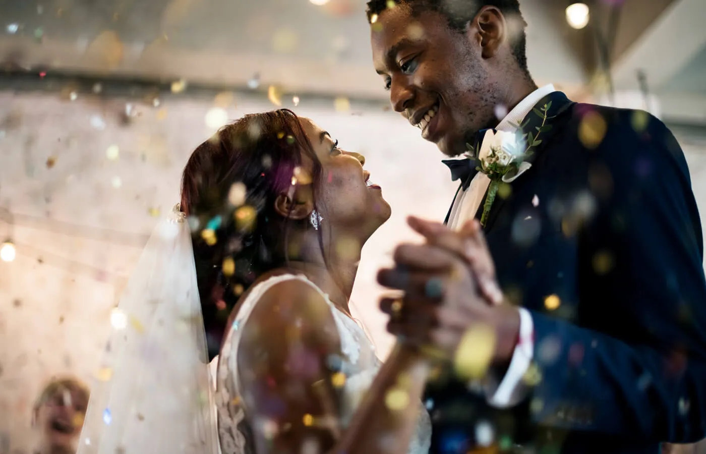 A newly married couple dancing at their wedding reception with confetti falling around them.