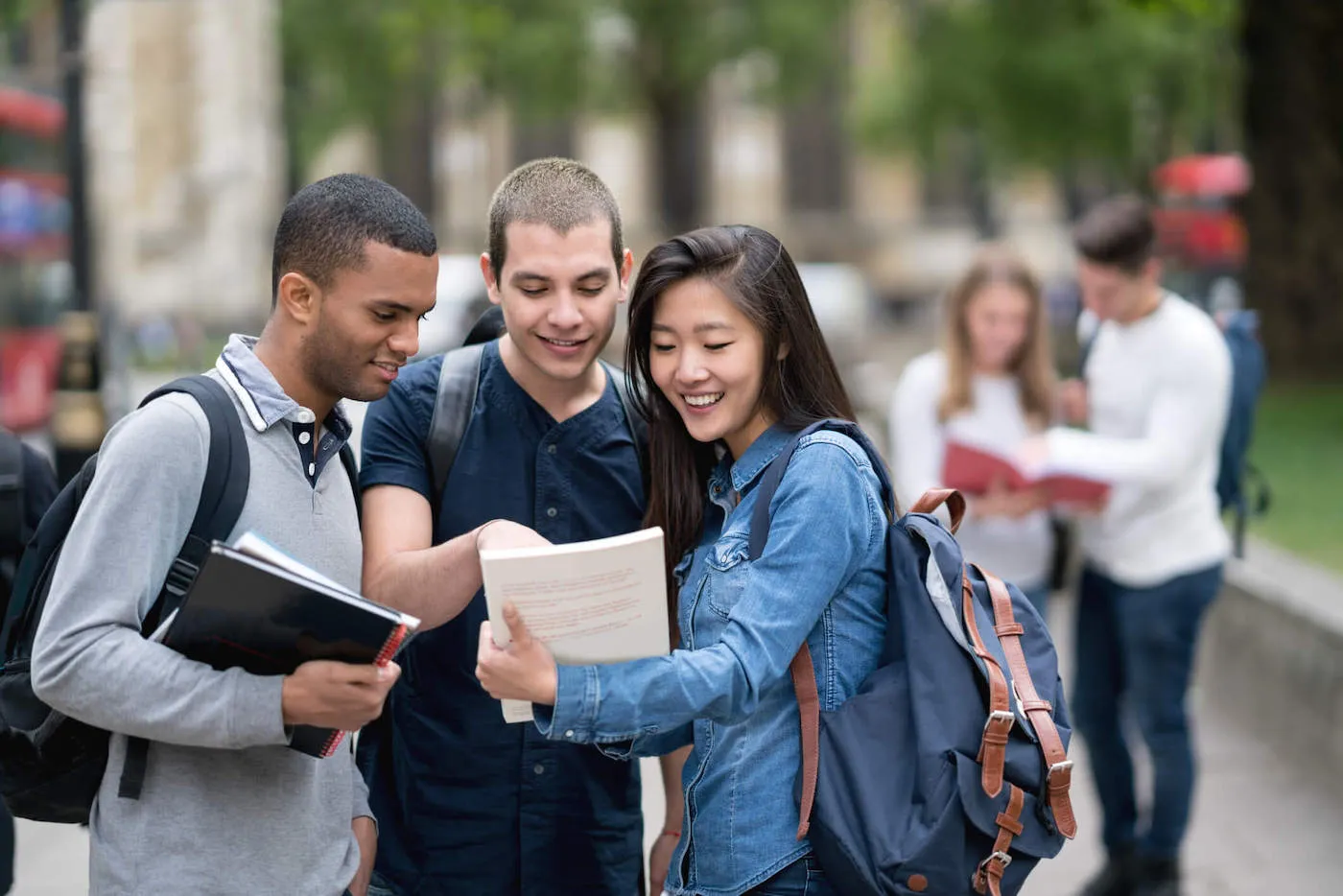 A group of three college students smile together while looking at a textbook outside.