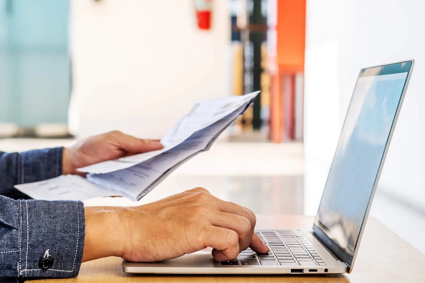 hands holding paper and typing on laptop