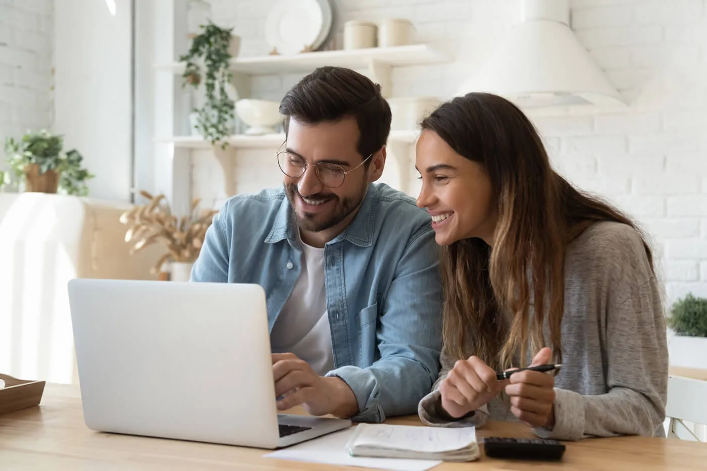 Happy young couple husband and wife using laptop computer looking at screen pay bills online in app calculate mortgage investment payment on website planning budget discuss finances sit at home table