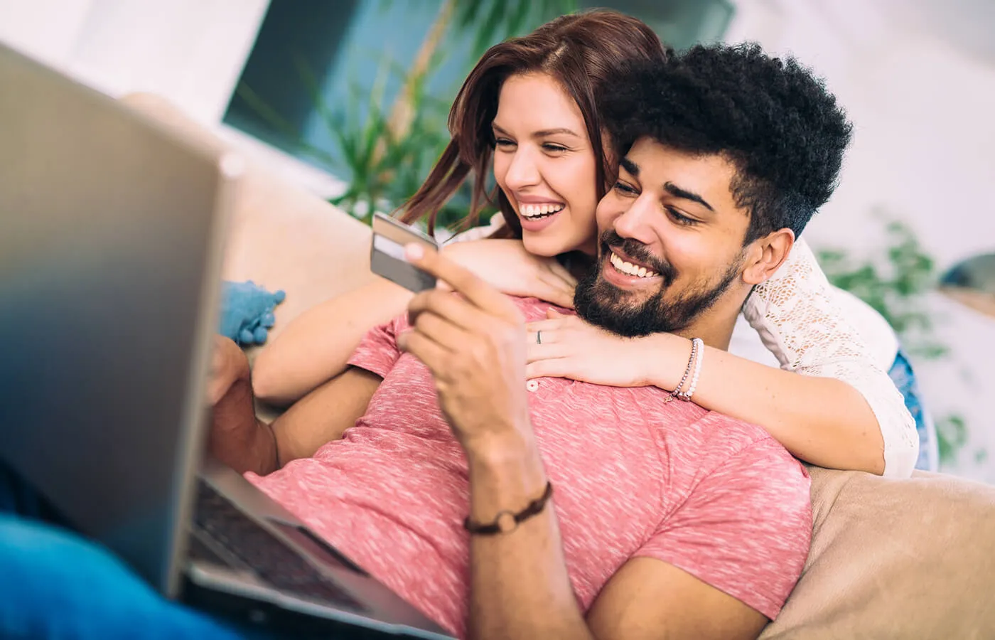 A happy couple on the sofa looking at the credit card and the laptop monitor, the woman is hugging the man