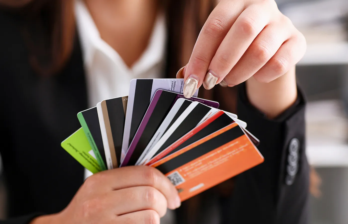 Woman holding multiple credit cards fanned out in one hand, pulling one out of the middle of the stack.