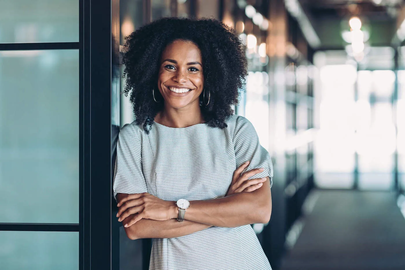 A woman with crossed arms leaning against a wall, smiling.