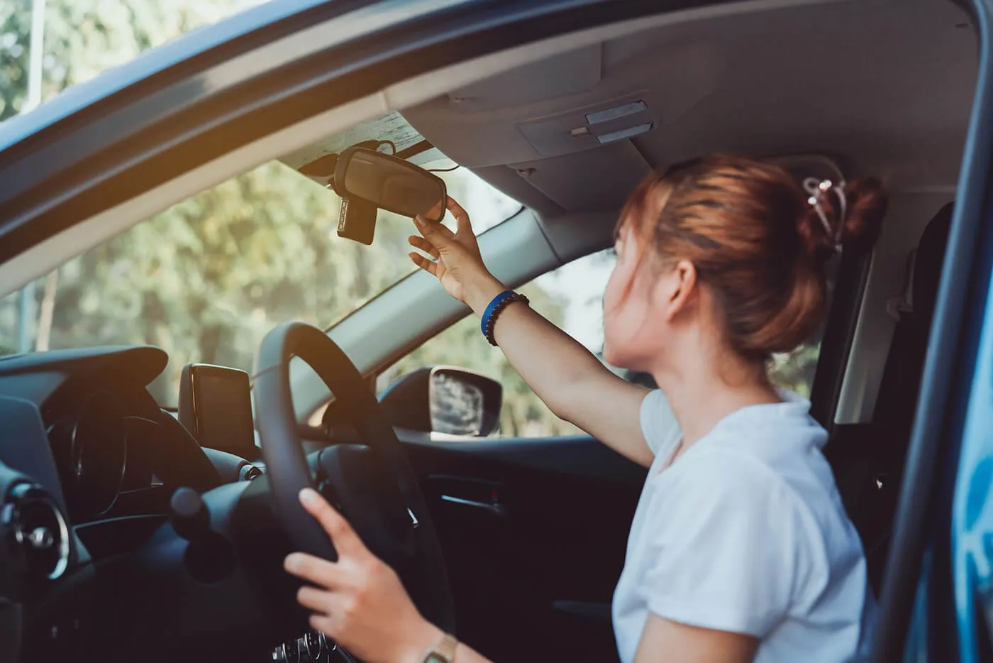 A woman adjusting the car rearview mirror in her car's interior before driving.