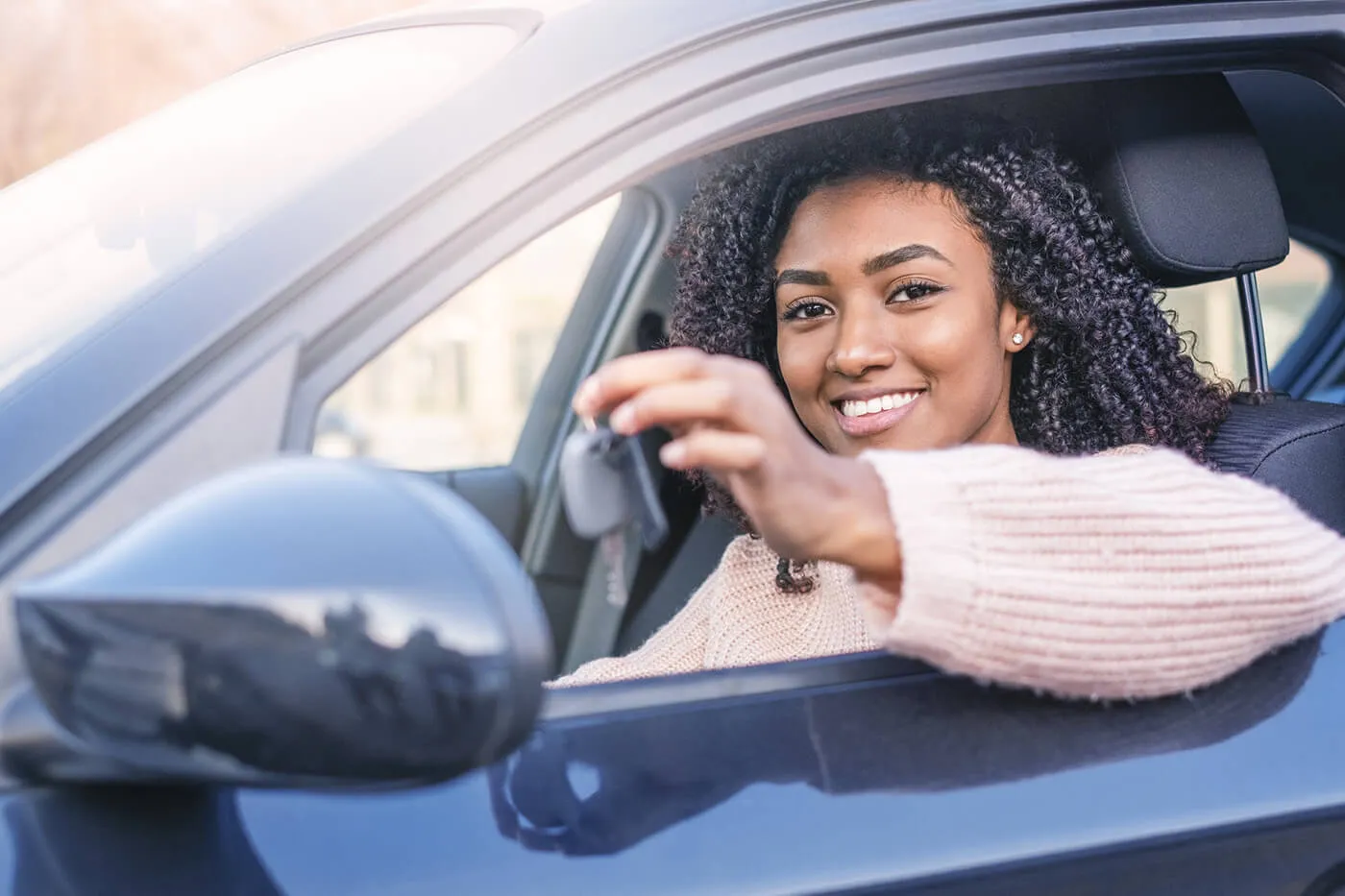 Young woman at the wheel on her new car, holding key.