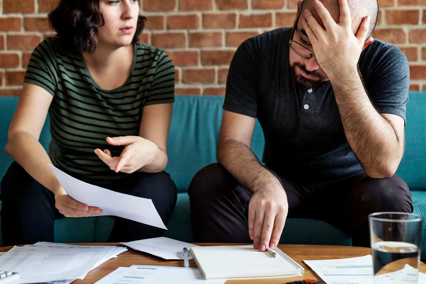 A stressed couple working on finances in their home. They are reading documents while sitting on their couch.