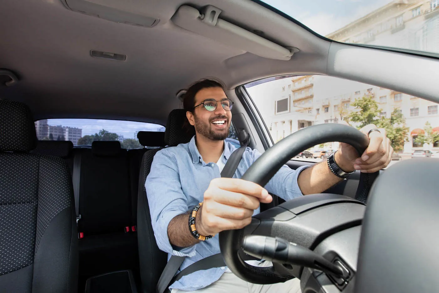 A man wearing a blue shirt smiles while driving his car on the street.