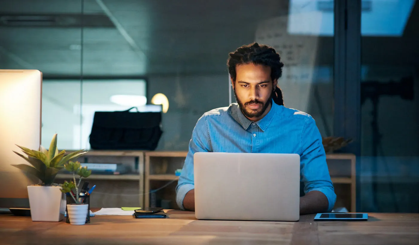 A man wearing a blue shirt types on his laptop computer while at the office.