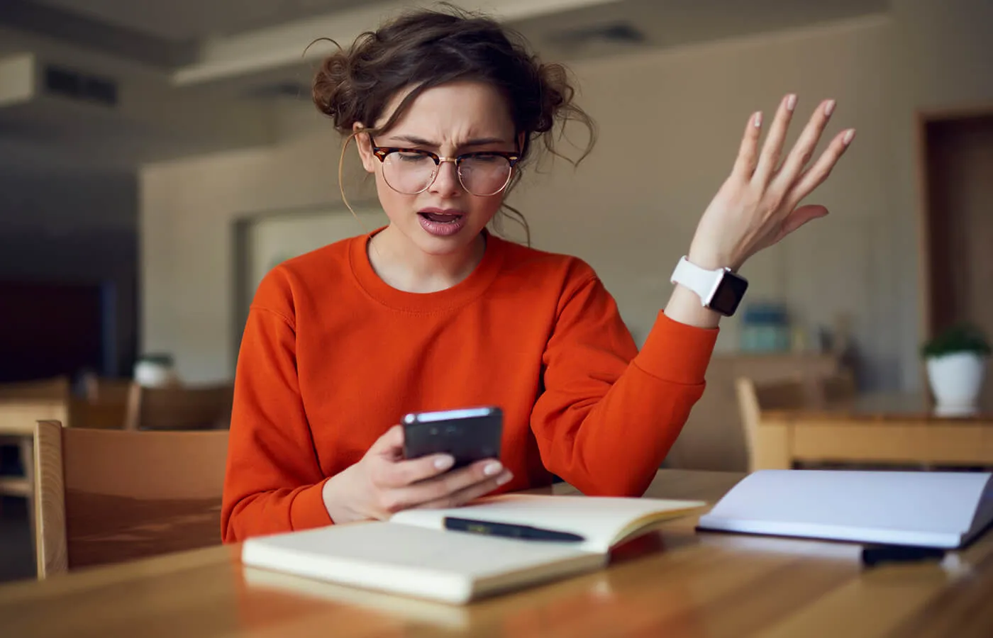 woman with glasses in orange shirt on a brown table with an open book