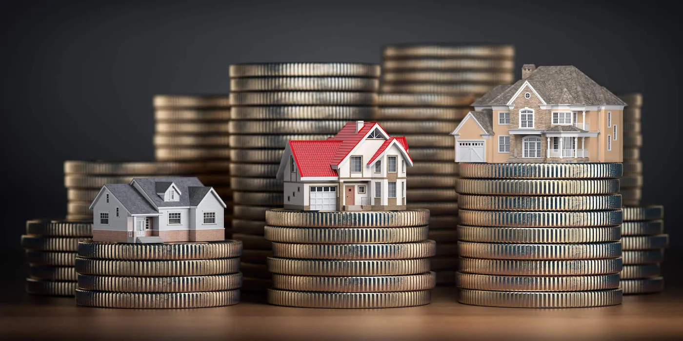 A set of three miniature home models sit on top of coins.