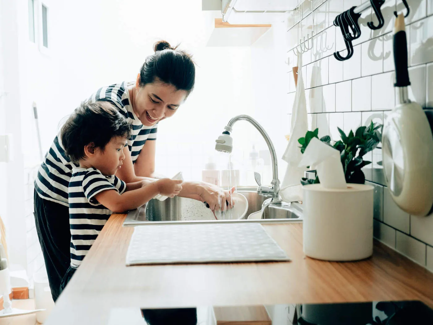 A mother smiles at her son as they clean the dishes at home