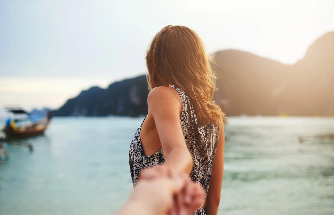 woman reaching back for hand while looking at sea.