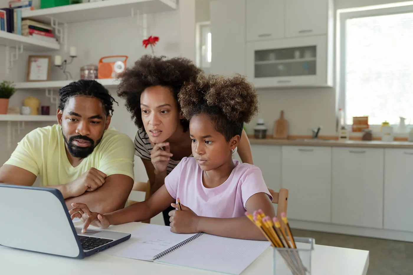 A family of three using a laptop in the kitchen