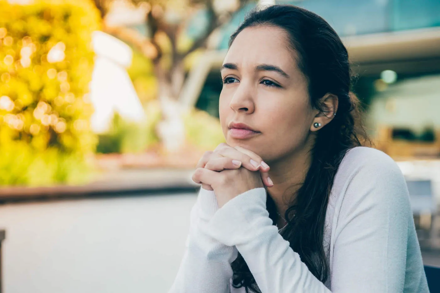 Portrait of pensive or sad young woman sitting at sidewalk cafe.