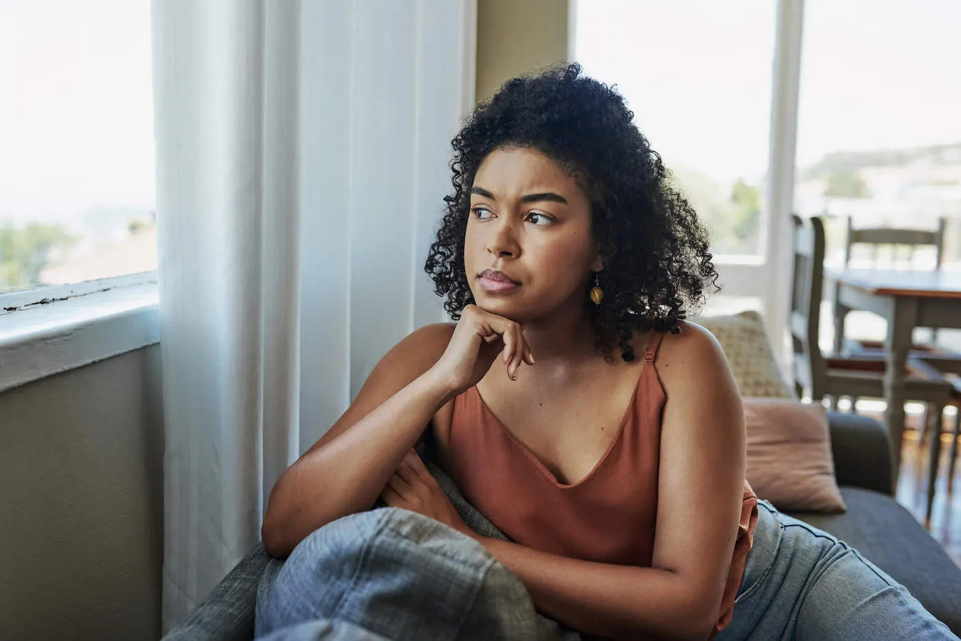 Shot of a young woman looking pensively out a window at home.