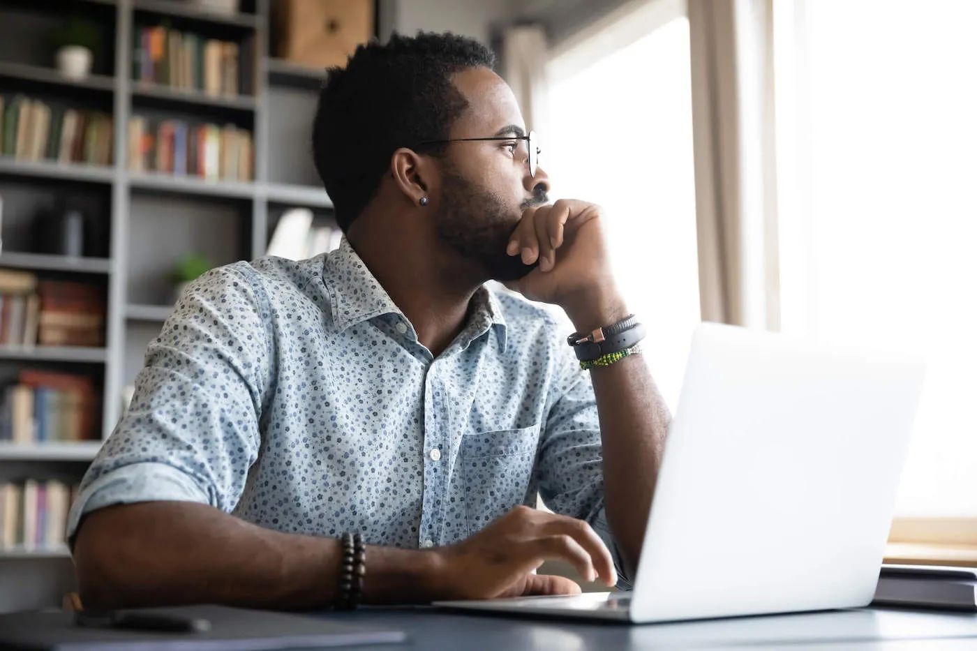 Thoughtful serious african man sit with laptop thinking of project.