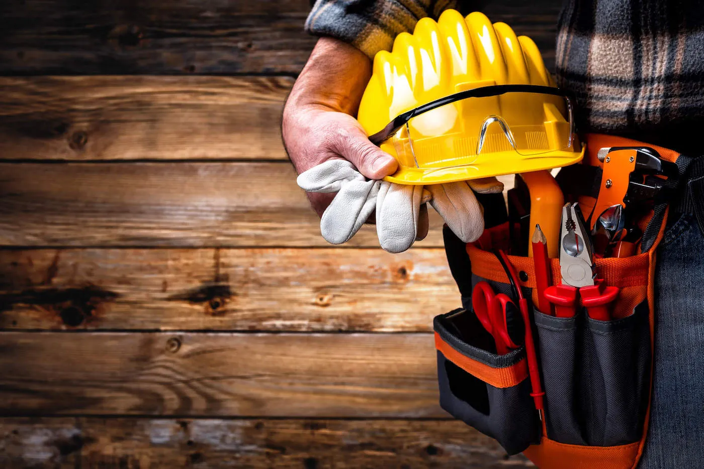 A utility worker holds his safety hat, gloves, and glasses next to his tool pouch.