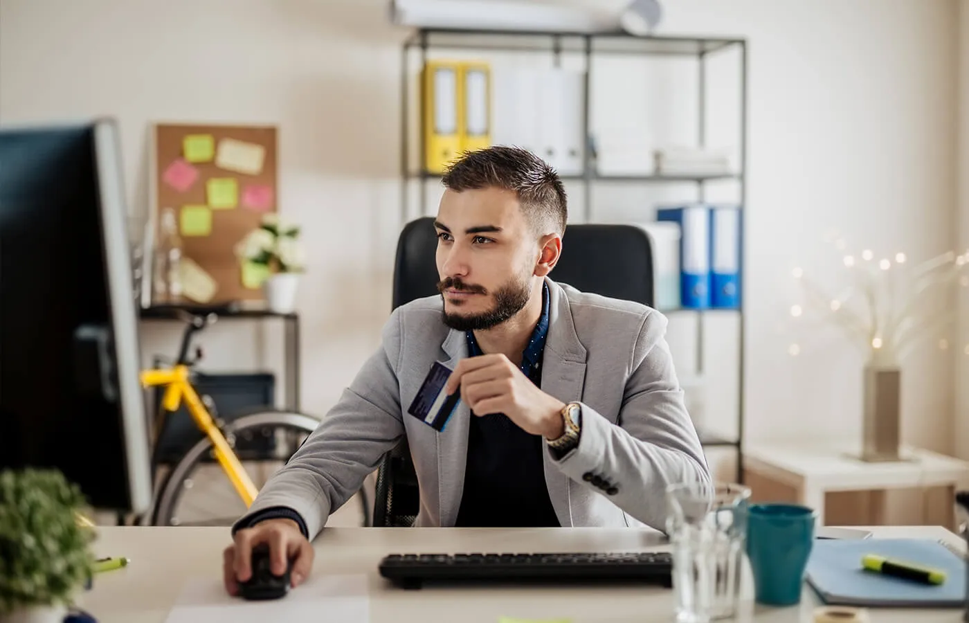 A man looking at his desktop computer in his office, learning about the common types of credit card fees.