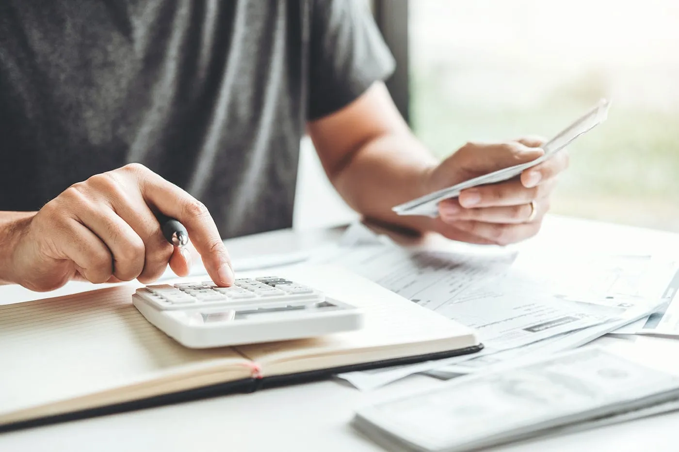 A person uses a calculator while holding cash in their other hand.