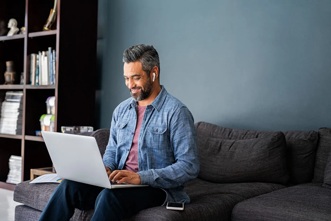 man in demin jacket seating on a couch with a laptop typing